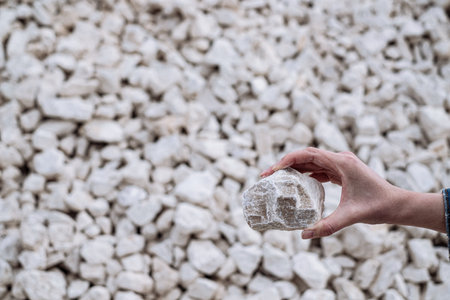 Hand holds a white chalkstone with a lot of stones on the backgroundの写真素材