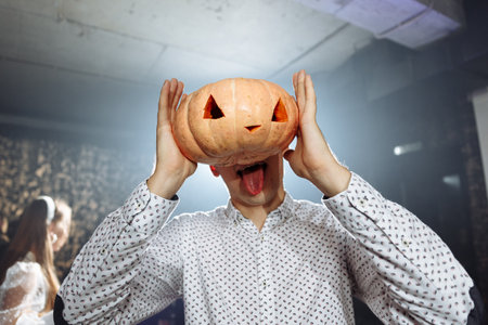Halloween pumpkin. Unrecognizable man holding in hand a scary face pumpkin instead his face.の写真素材