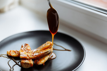Teaspoon drops caramelized syrup onto banana on black plate white table, vegan dessert. Selective focusの写真素材