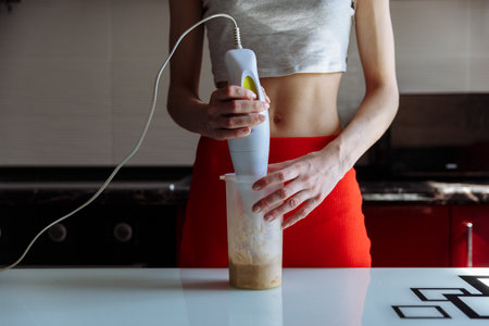 Woman with hand blender making sweet banana protein shakeの写真素材