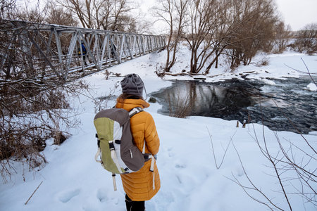 Hiking tourist is standing before the river with a bridge. Winter Viewの写真素材