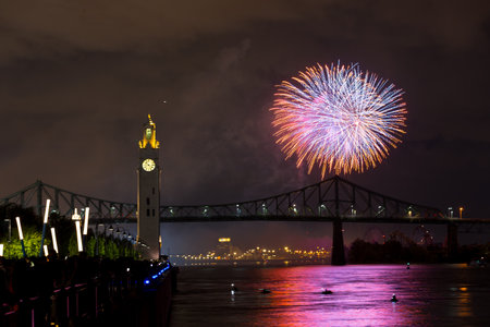 Montreal Clock Tower and Jacques Cartier Bridge with fireworks at night during summer celebration....