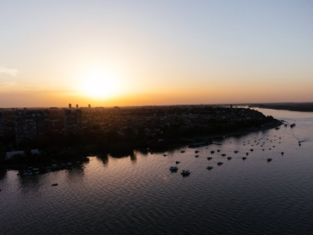 Aerial view of riverbank with boats and city skyline at golden hour. g .