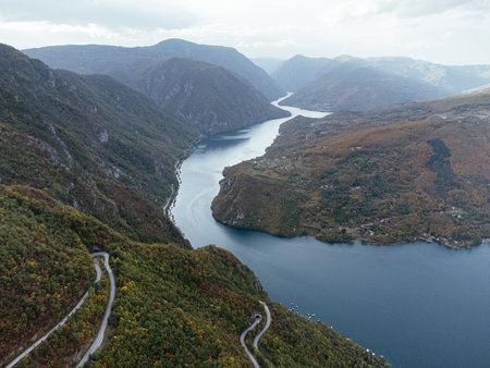 Aerial view of winding mountain road beside river in autumn valley. g.