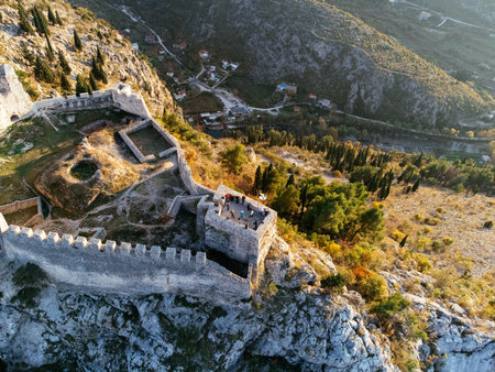Aerial view of Ljubushki Fortress on a rocky hill at sunset, surrounded by rugged mountains and forested valley. g.の写真素材