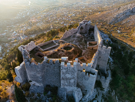 Aerial view of Ljubushki Fortress on a rocky hill at sunset, surrounded by rugged mountains and forested valley. g.の写真素材