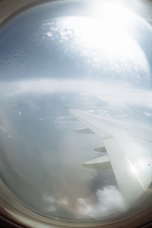 View from airplane window with wing above clouds and blue sky.