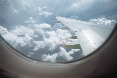 View from airplane window with wing above white fluffy clouds and blue sky.の写真素材