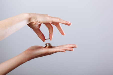 Woman's hand is taking a coin from another hand on isolated white background, crisis concept.の写真素材