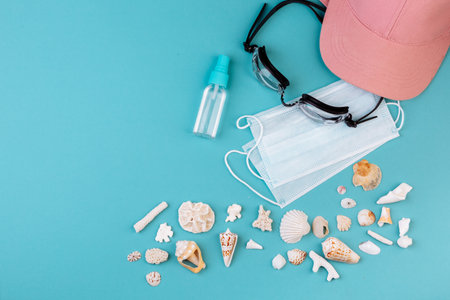 Vacation: Protection mask, cap, swimming goggles, different kinds of seashells are lying on the blue background.の写真素材