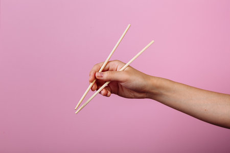 Hands holding chopsticks. Isolated on pink background, the place for caption and text.の写真素材