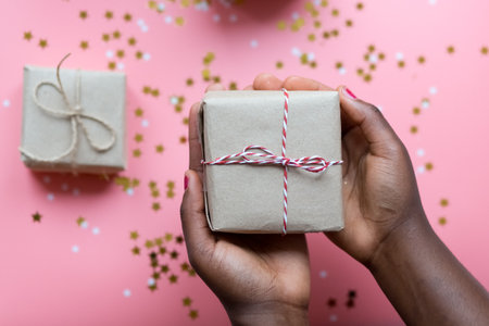 African woman hands is holding present box on pink background with stars and snowflakes confetti.の写真素材