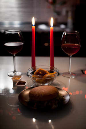 Two red wine glasses with lit candles behind, warm bokeh lights and romantic mood.の写真素材