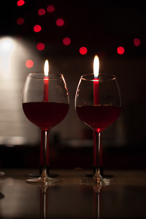 Two red wine glasses with lit candles behind, warm bokeh lights and romantic mood. g.の写真素材
