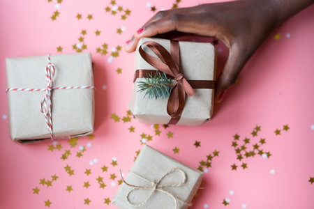 African woman is holding a brown gift box with a pink ribbon on a festive pink background with...