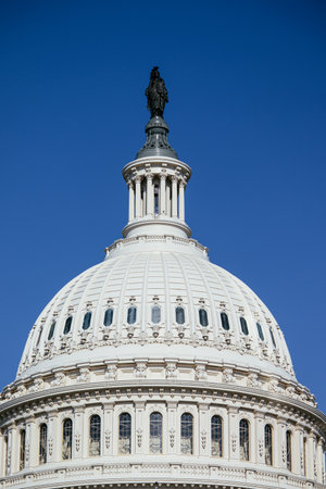 United States Capitol building with iconic dome and American flag under clear blue sky in Washington...