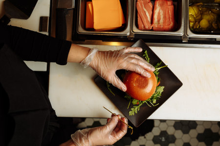 Chef hands in gloves assembling vegan burger with plant based patty and fresh arugula in restaurant kitchen. g.の写真素材