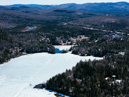 defaultAerial view of winding road along frozen lake in Quebec with forest and mountains under blue sky. g.の写真素材