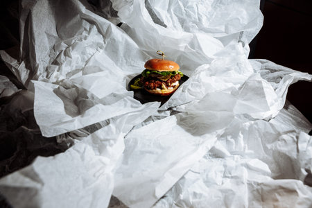 Vegan burger with plant based patty on black plate surrounded by crumpled white paper in dark studio...