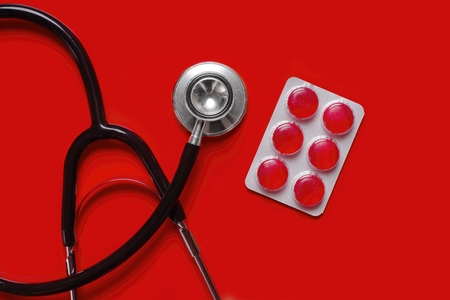 Stethoscope and medicine pills on red background with copy space.の写真素材