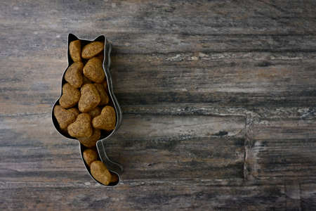 Cat shaped cookie cutter filled with heart shaped cat food on a wooden plate.の写真素材