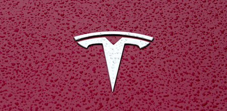 Ulm, Baden-wuerttemberg, Germany - October 19, 2021: Close up of a Tesla car logo on red metallic surface with rain drops.のeditorial素材