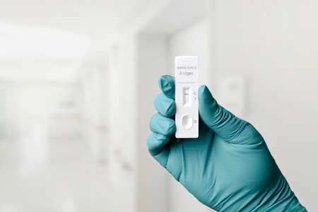 Gloved hand holding a rapid test device for COVID-19 with negative test result.