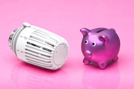 Piggy bank next to thermostat for heating home with pink background. Rising costs for heat and energy concept.の写真素材