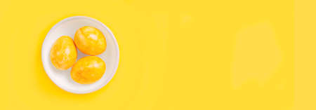 Decorative painted easter eggs in a white bowl on yellow background. Panoramic image with copy space.の写真素材