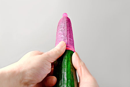 Unrecognizable person pulls a condom over a cucumber.