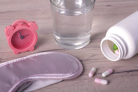Alarm clock next to a glass of water and sleeping pills on a table. Insomnia concept.の写真素材