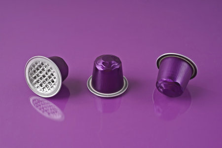Disposable coffee capsules over purple background with copy space.