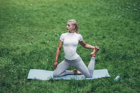 Fitness Woman Preparing for Yoga in the Early Morning Park. Wearing Stylish Sport Outfit. Blue Bottle of Water and Yoga Mat. Healthy Lifestyle.の写真素材