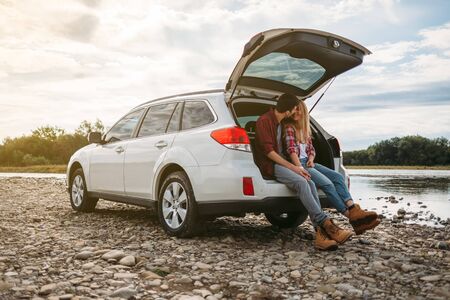 Young travel couple sitting in the trunk of his car near the carpathian river Stryiの写真素材