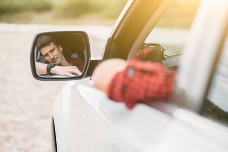 Young man driver looking in car side view mirror, making sure line is free before start moving. Positive human face expression emotions. Safe trip journey driving conceptの写真素材