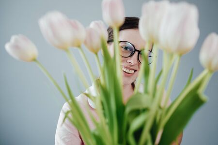 Studio Portrait of Young Adult Pretty Girl with Glasses Dressed in Pink T-shirt Holds Bouquet of Fresh Tulipsの写真素材