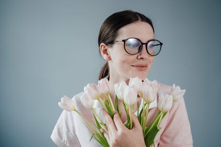 Studio Portrait of Young Adult Pretty Girl with Glasses Dressed in Pink T-shirt Holds Bouquet of Fresh Tulipsの写真素材