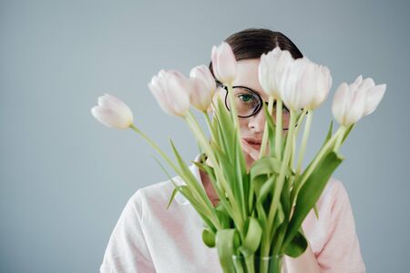 Studio Portrait of Young Adult Pretty Girl with Glasses Dressed in Pink T-shirt Holds Bouquet of Fresh Tulipsの写真素材