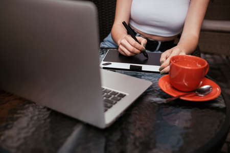 Young Woman Working on Laptop and Drawing Tablet While Sitting in Cafe Outdoors, Freelance Conceptの写真素材