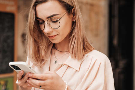 Close Up Portrait of Confident Young Woman with Eyeglasses Texting on Smartphone While Walking in...
