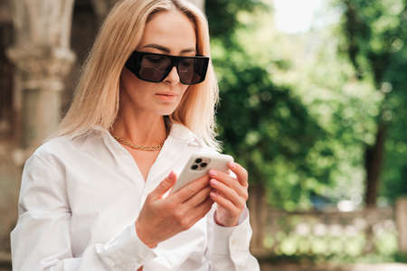 Close Up of Confident Woman Texting on Smartphone While Standing on the Street, Elegant Businesswoman Wearing Sunglasses Looking to the Mobile Phoneの写真素材