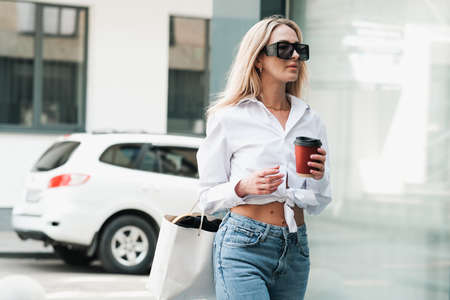 Elegant Blonde Woman Holding Cup of Coffee in Hand and Looking Away, Confident Female Entrepreneur...