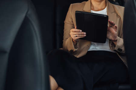 Unrecognisable Female Entrepreneur Working on Tablet While Sitting on Back Seat of a Carの写真素材