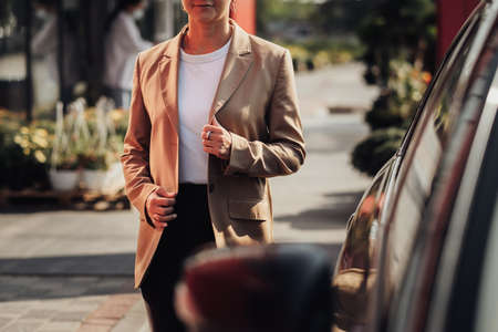 Unrecognisable Stylish Woman in Brown Jacket Moving Near the Car