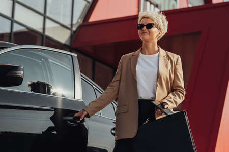 Elegant Female Entrepreneur with Briefcase in Hand Opening Door of the Luxury Carの写真素材