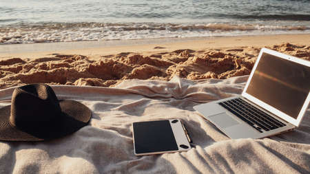 Close Up View of Laptop, Tablet and Hat Lying on the Plaid on Sandy Beach by the Sea, Freelance Concept, Remote Workingの写真素材