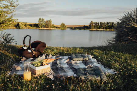 Picnic Set Outdoors by the Lake at Sunset, Child Car Seat, Fruit Basket and Bottle of Juice on Plaidの写真素材