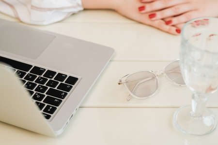 Close Up of Unrecognisable Woman Sitting by a Table with Laptop, Glass of Water and Glasses, Freelance Conceptの写真素材
