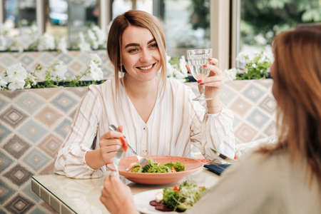 Cheerful Young Woman Having Lunch with Her Female Friend in the Restaurantの写真素材