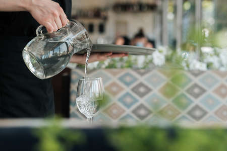 Close Up of Female Waiter Pouring Water to the Glass in Restaurantの写真素材
